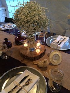 the table is set with silverware and flowers in mason jar vases on wood slices