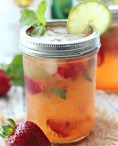 two mason jars filled with liquid and strawberries next to limes on a table