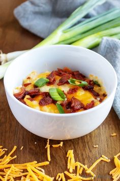 a bowl filled with cheese and bacon on top of a wooden table next to celery