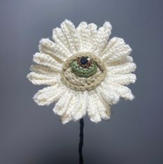 a crocheted white flower with an eye on it's center, sitting in front of a gray background