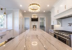 a large kitchen with marble counter tops and white cabinets, along with a chandelier hanging from the ceiling