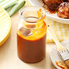 a jar of bbq sauce sitting on top of a table next to plates and utensils