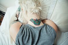 a woman laying in bed with her back turned to the camera and a butterfly tattoo on her neck