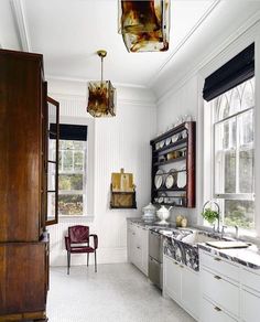 a kitchen with white cabinets and marble counter tops, along with an antique style chandelier