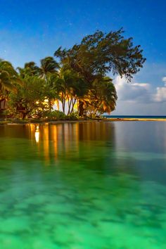 an island with palm trees in the background and water reflecting it's lights at night