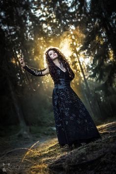 a woman in a long dress standing on a tree stump with her arms outstretched and sun shining through the trees behind her