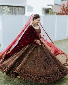 a woman in a red and gold bridal gown is posing for the camera with her veil draped over her head