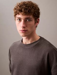 a young man with curly hair is looking at the camera while wearing a brown shirt