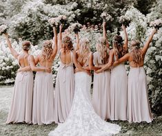 a group of women standing next to each other in front of flowers and greenery