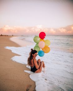 a woman sitting on the beach holding balloons