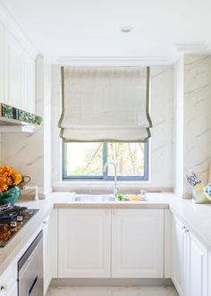 a kitchen with marble counter tops and white cabinets, along with a window covered in roman shades