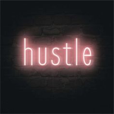 the word hustle is lit up in pink on a dark brick wall with a black background