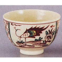 a white bowl with red and green designs on the rim, sitting on a gray surface