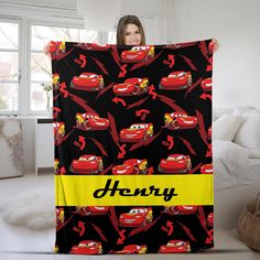 a woman holding up a blanket with cars on it and the name henry printed on it