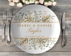 a white plate with gold lettering and flowers on it next to silverware, forks and knives