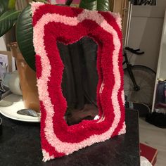 a red and white frame sitting on top of a table next to a plant in a vase