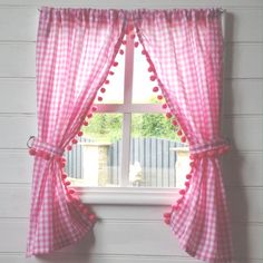 a window with pink checkered curtains and pom poms on the top curtain