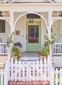 a white house with a green door and some flowers on the front porch, next to a white picket fence