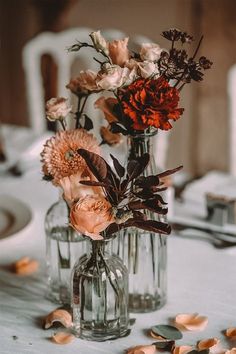 two vases filled with flowers sitting on top of a white tablecloth covered table