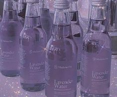 six bottles of lavender water are lined up on a table with sparkles in the background