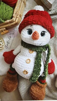 a crocheted snowman with a red hat and green scarf sitting on top of a white blanket