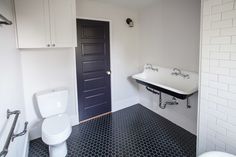 a white toilet sitting next to a black and white sink in a bathroom on top of a tiled floor