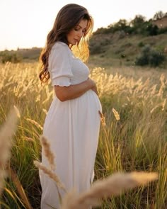 a pregnant woman standing in tall grass at sunset