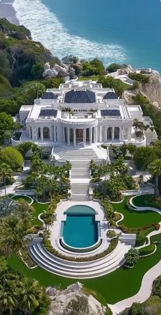 an aerial view of a large white mansion with a pool in the foreground and ocean in the background