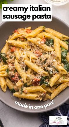 pasta with sausage and spinach is served in a gray bowl on a white table