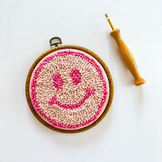 an embroidered smiley face on a wooden hoop next to a crochet hook and needle