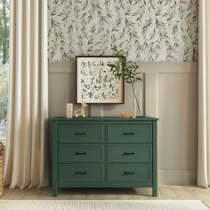 a green dresser sitting in front of a window next to a wall with leaves on it