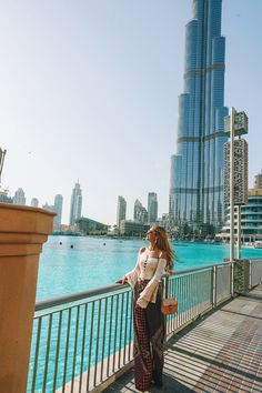 a woman is standing on a bridge looking at the water in front of some tall buildings