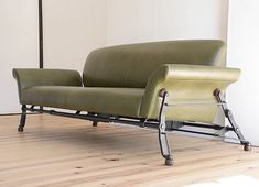 a green couch sitting on top of a hard wood floor next to a white wall