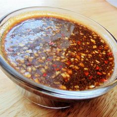 a glass bowl filled with chili sauce on top of a wooden table next to a knife and fork