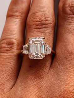 a woman's hand holding an emerald and diamond ring