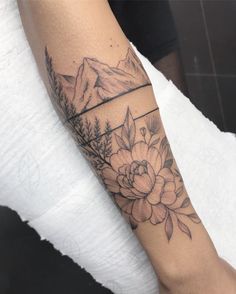 a woman's arm with flowers and mountains in the background on her left forearm