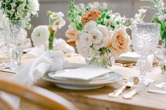 the table is set with white and peach flowers in vases, napkins, and silverware