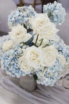 a bouquet of white and blue flowers in a vase on a tableclothed cloth