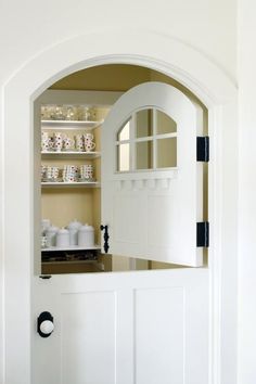 an open white door leading to a kitchen with dishes on the shelves and in front of it