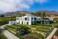 an aerial view of a large white house surrounded by greenery and palm trees with mountains in the background