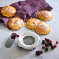 some pies and berries on a table with a purple cloth next to them,