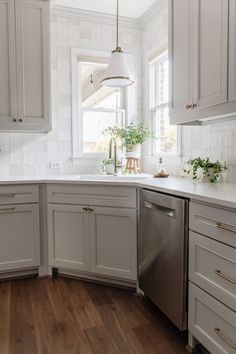 a kitchen with white cabinets and wood floors is pictured in this image, there are plants on the window sill