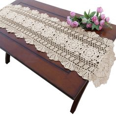 a wooden table topped with a white doily next to pink flowers on top of it