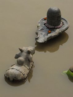 three statues in the water near a boat with a bell on it and a statue of an elephant next to it