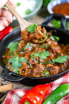 a person holding a spoon full of chili and meat in a cast iron skillet