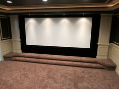 an empty theater room with carpeted flooring and two large screens on the wall