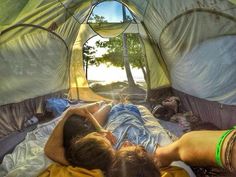 two people laying in a tent with the sun shining through it's windows and trees