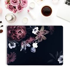 an apple laptop computer sitting on top of a desk next to flowers and other items