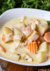 a white bowl filled with chicken and dumplings on top of a wooden table next to carrots