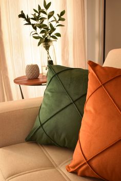 two orange and green pillows sitting on top of a couch next to a vase with a plant